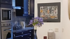 A wooden dining table with orange placemats, a vase with purple flowers, and a framed abstract painting on the wall.