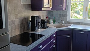 A modern kitchen with purple cabinets, a built-in stove, and a window with a view of greenery.