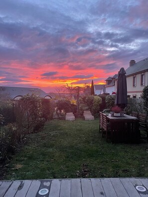 Un jardin avec une terrasse en bois, une table et des chaises, et un espace patio couvert.