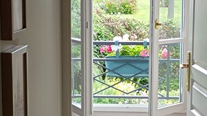 A doorway leading to a balcony with a view of a garden and a blue chair.