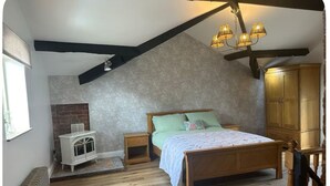 A bedroom with a sloped ceiling, a wooden bed, a nightstand, a chest of drawers, and a radiator. - The Hurst Stable, 1800 century Coach House offering luxurious amenities, Hottub (Wheaton Aston)