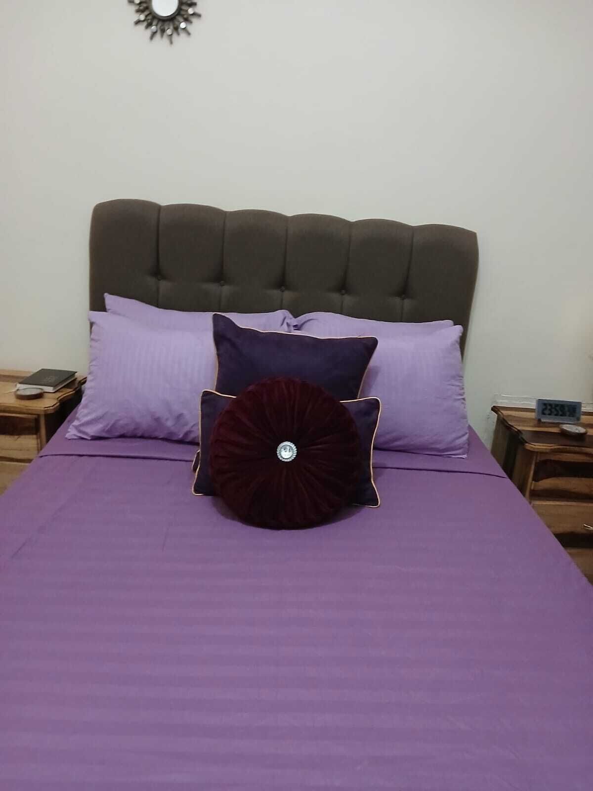 Un lit avec une couvre-lit violette et trois oreillers de différentes nuances.