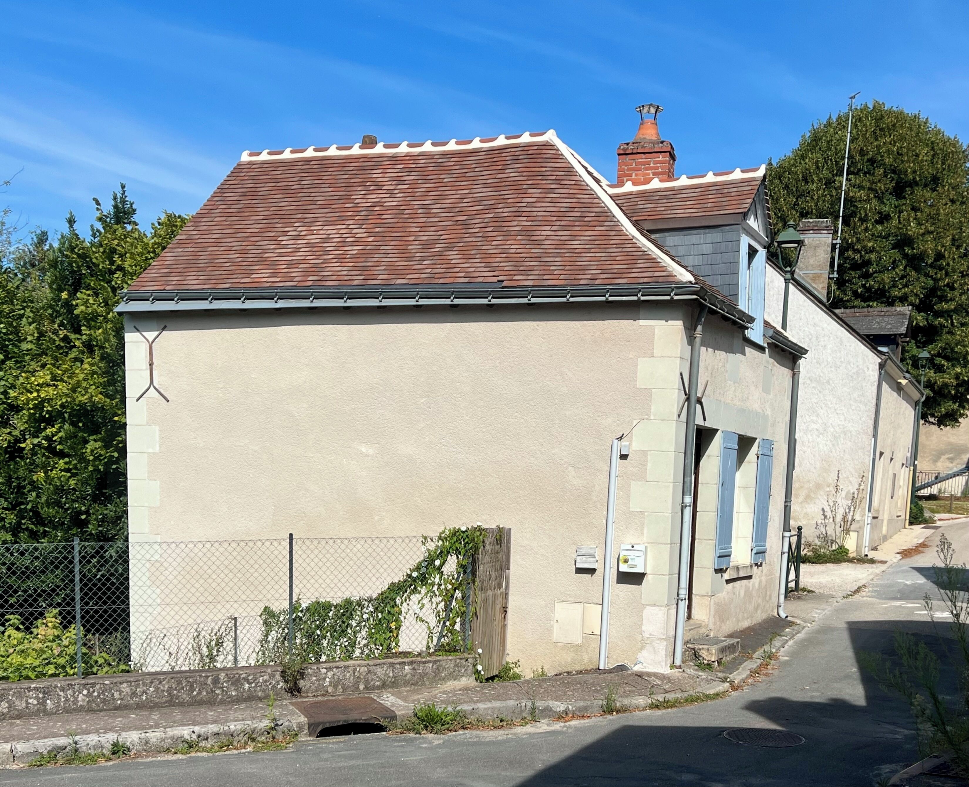 Ein zweistöckiges Gebäude mit rotem Ziegeldach, beige-farbenen Wänden und blauen Fensterläden.