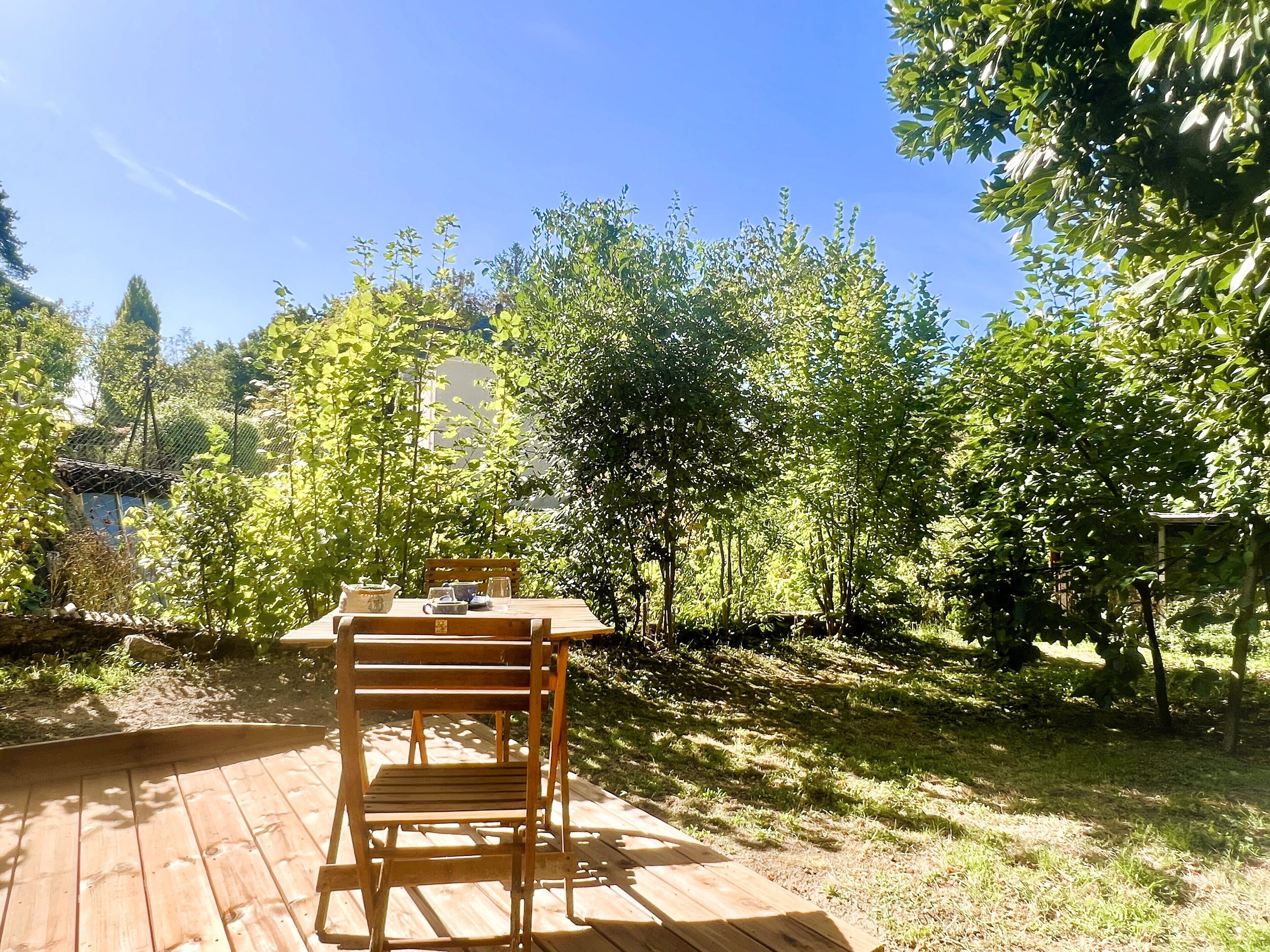 A wooden deck with a table and chairs, surrounded by lush greenery and trees.