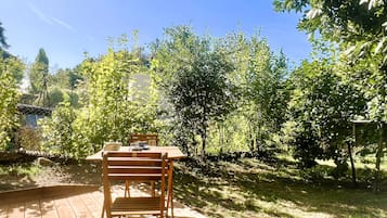 A wooden deck with a table and chairs, surrounded by lush greenery and trees.