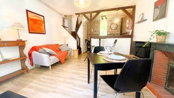 A dining area with a table set for two, a sofa with an orange throw, and a staircase leading to another level.