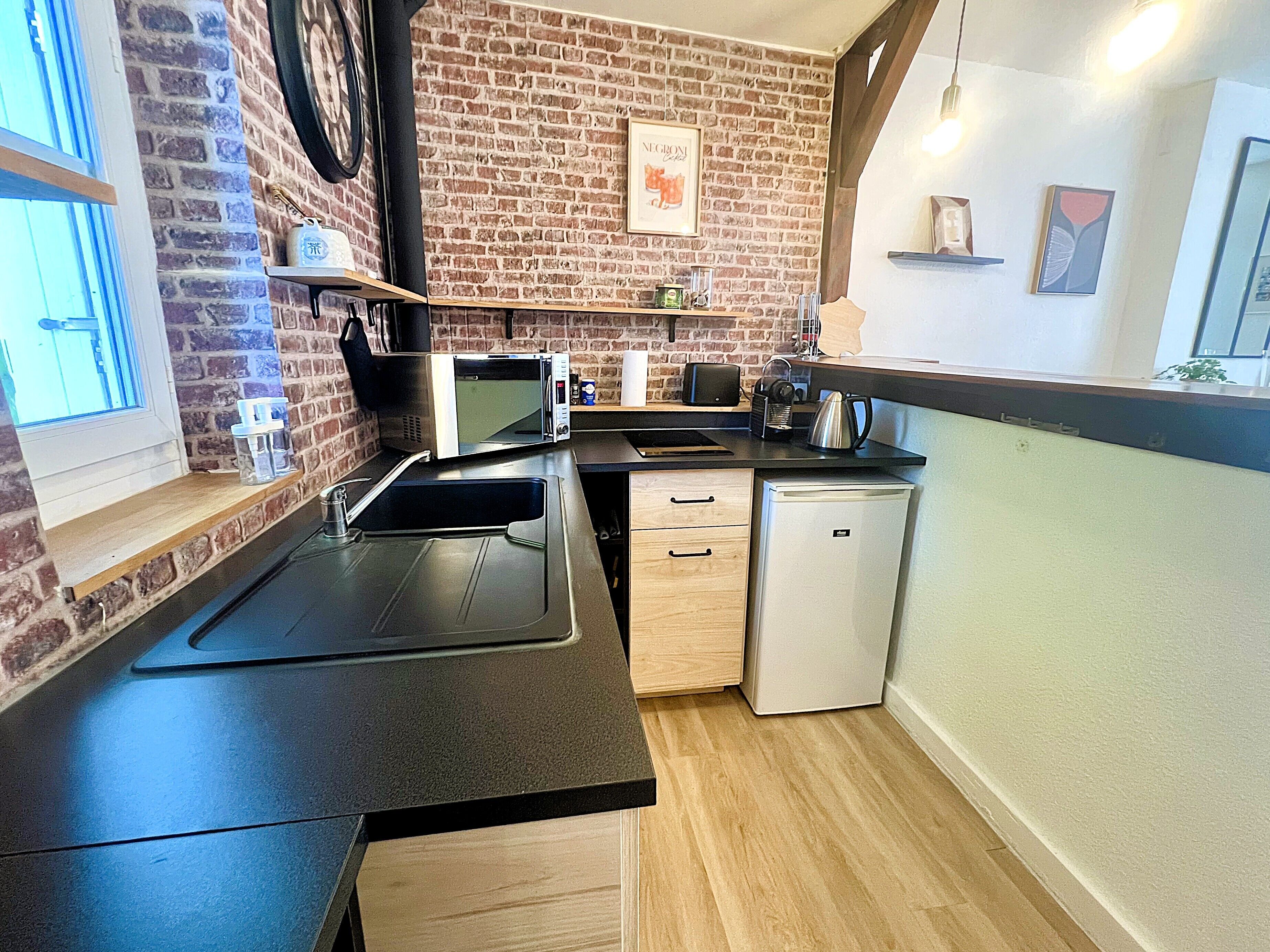 A compact kitchen with a brick wall, a microwave, a small refrigerator, and wooden cabinets.