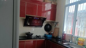 A compact kitchen with red cabinets, a gas stove, a black frying pan, and a window with a view of buildings. - Wangxian Valley Morning Wind B&B - Wangxian Valley Scenic Area (Shangrao)