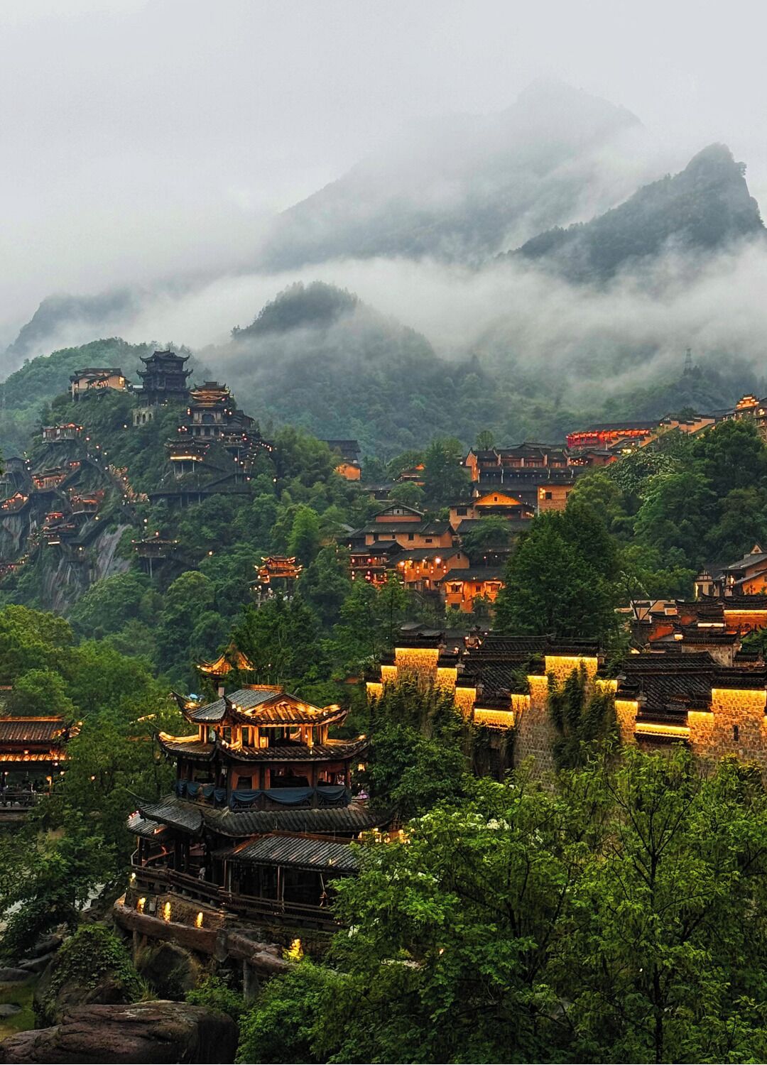 A traditional village with tiered buildings, surrounded by lush greenery and mountains.