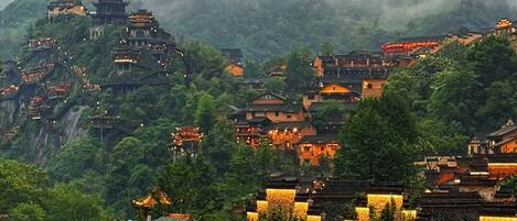 A traditional village with tiered buildings, surrounded by lush greenery and mountains.