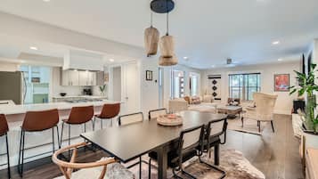 A modern kitchen with white cabinets, a dining area with a dark wooden table and chairs, and a living room with a sofa and decorative items.