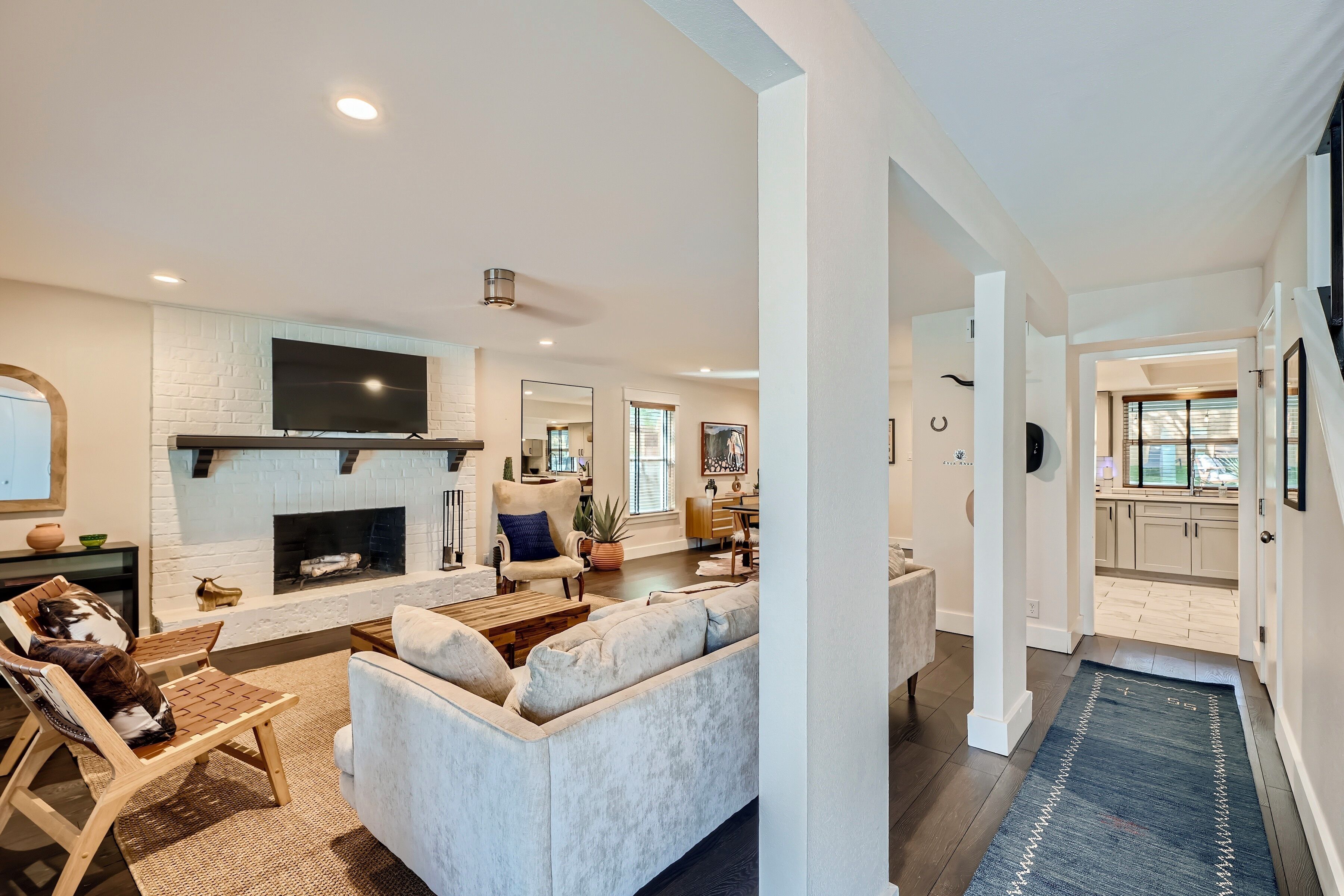 A modern living room with a fireplace, a flat-screen TV, and a dining area with a kitchen in the background.