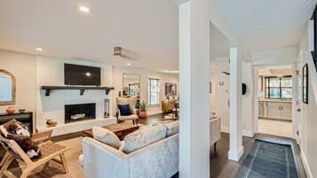 A modern living room with a fireplace, a flat-screen TV, and a dining area with a kitchen in the background.
