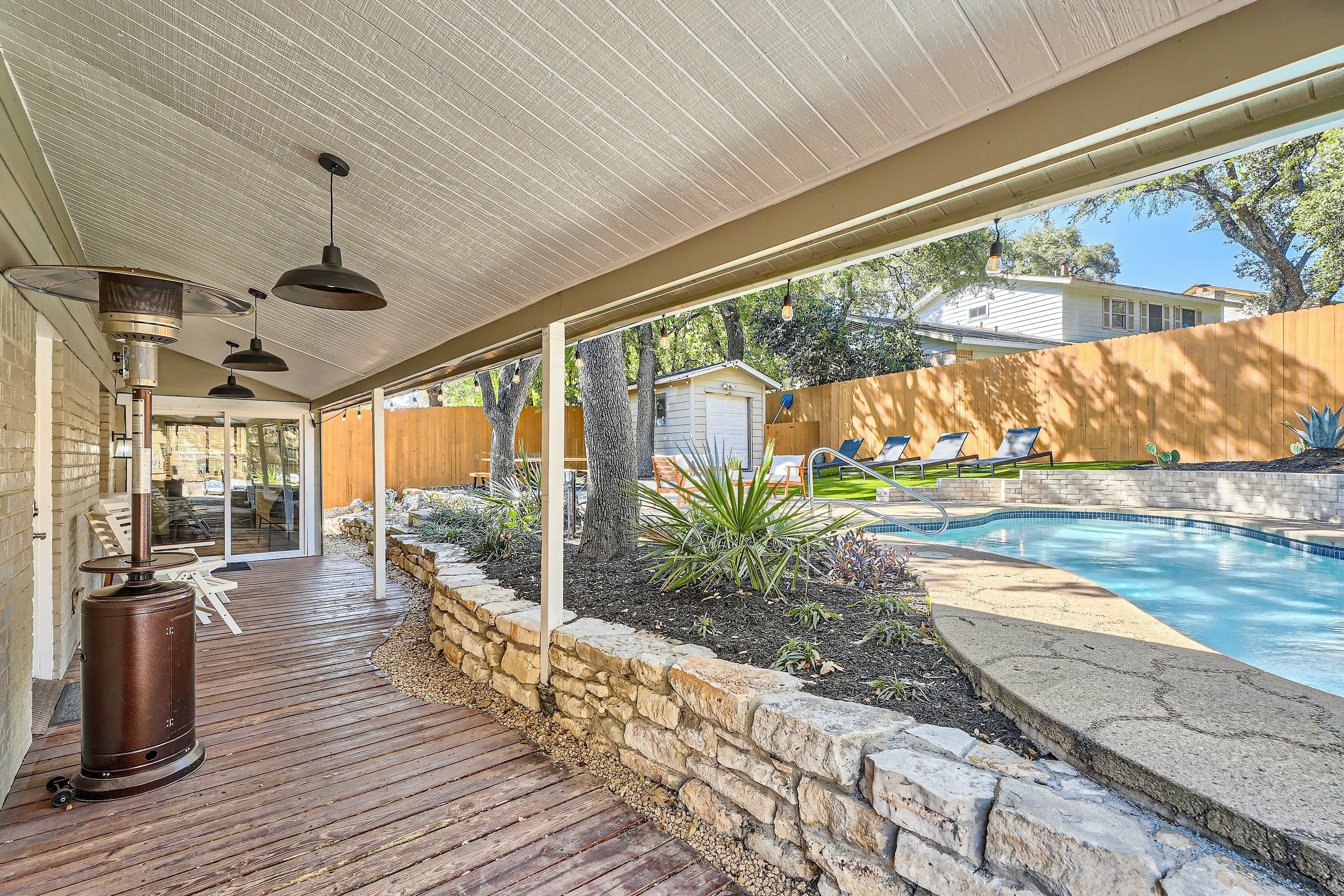 A covered patio area with a pool, stone walls, and outdoor furniture.
