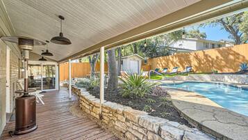 A covered patio area with a pool, stone walls, and outdoor furniture.