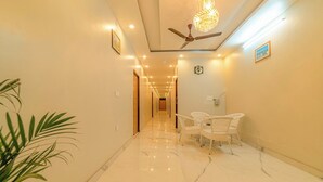 A hotel hallway with marble flooring, a ceiling fan, and white wicker chairs. - Hotel Rudra (Rishikesh)