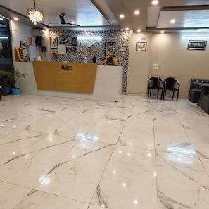 A reception area with a marble floor, a reception desk, and a wall decorated with various items. - Hotel Rudra (Rishikesh)