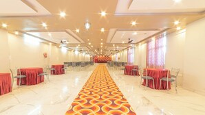 A long, well-lit corridor with rows of tables and chairs, a patterned carpet, and ceiling lights. - Hotel Rudra (Rishikesh)