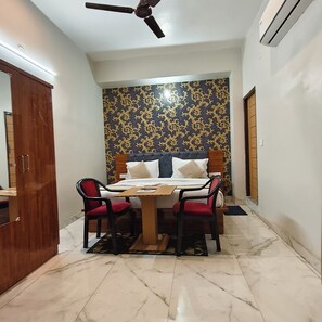 A bedroom with a bed, two chairs, a table, a ceiling fan, and an air conditioning unit.