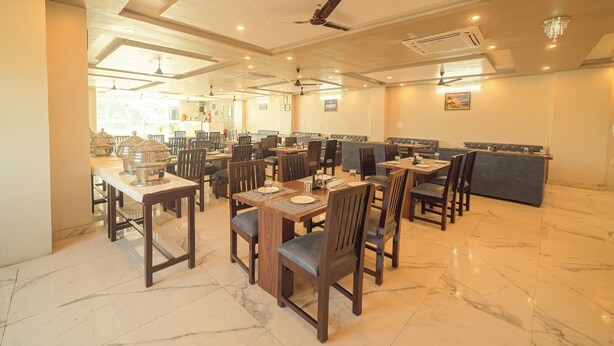 A spacious restaurant with multiple dining tables and booths, marble flooring, and ceiling fans. - Hotel Rudra (Rishikesh)