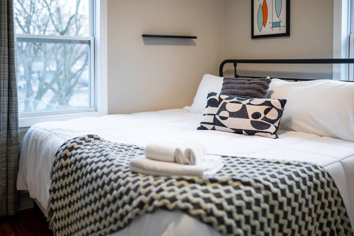 A neatly made bed with a patterned throw blanket, a pillow with a skull design, and a bedside table with a lamp.