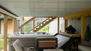 A hot tub area with a wooden deck, outdoor seating, and a staircase leading to a covered porch. - Private Basement - Two King Beds and Hot Tub (Saint Charles)