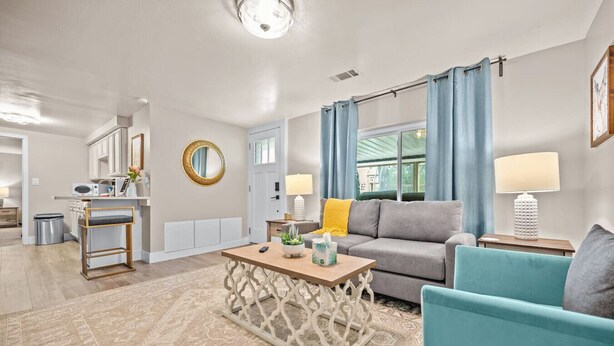 A modern living room with a grey sofa, teal armchairs, a wooden coffee table, and a patterned rug. - Private Basement - Two King Beds and Hot Tub (Saint Charles)