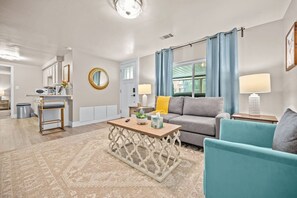 A modern living room with a grey sofa, teal armchairs, a wooden coffee table, and a patterned rug.