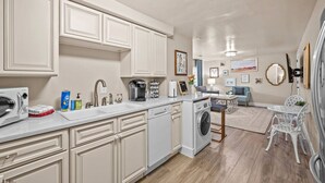 A modern kitchen with white cabinetry, a dishwasher, a washing machine, and a dining area with a table and chairs. - Private Basement - Two King Beds and Hot Tub (Saint Charles)