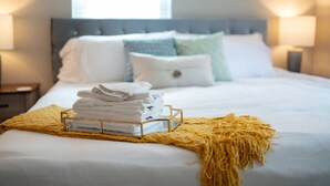 A neatly made bed with white linens, a gold tray with folded towels, and a yellow throw blanket. - Private Basement - Two King Beds and Hot Tub (Saint Charles)