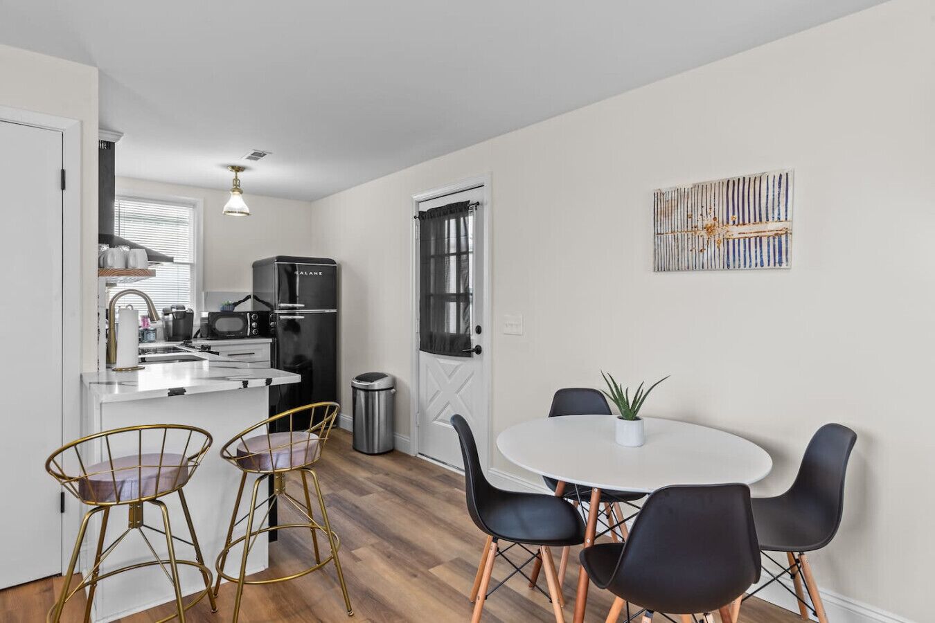 A compact kitchen with a refrigerator, sink, and modern bar stools.