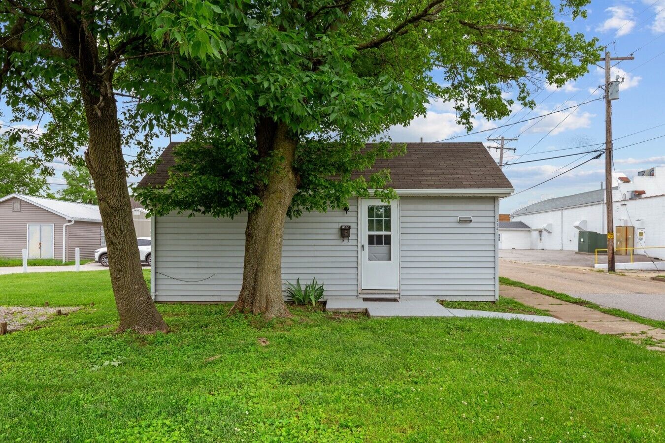 A small single-story house with a front door, a small porch, and a tree in front.
