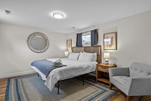 A hotel room with a bed, bedside tables, a chair, a mirror, and artwork on the walls. - Wentzville King Bed Walk to Downtown! (Wentzville)