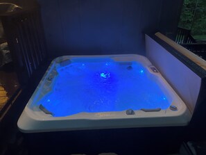 Ein Whirlpool mit blauem Licht, umgeben von einem dunklen Raum mit Holzboden und einem Fenster.