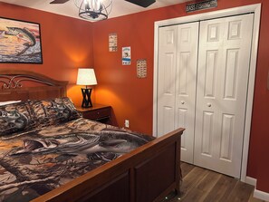 A bedroom with a bed, a nightstand, a lamp, a painting, and a closet.
