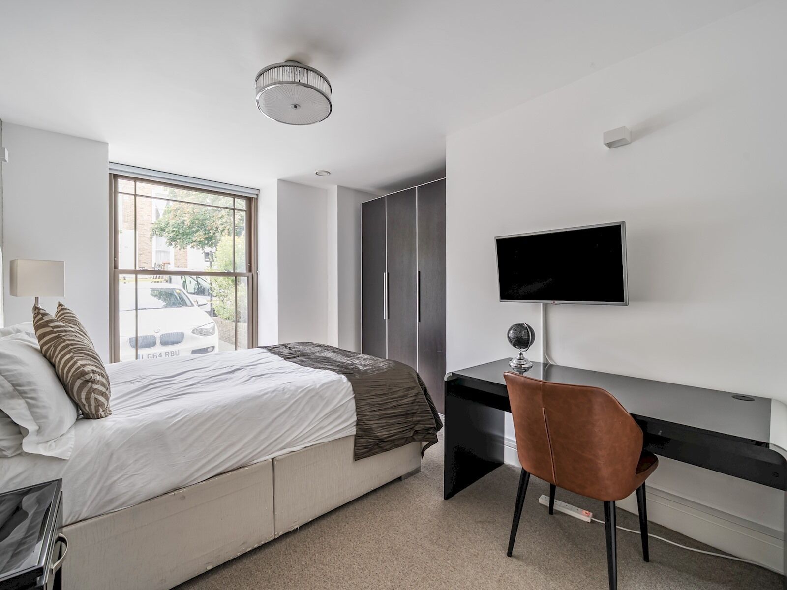 Un dormitorio con cama, escritorio, silla, televisor y ventana.