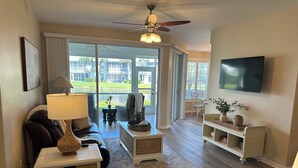 A spacious living room with a ceiling fan, a TV mounted on the wall, a comfortable sofa, a coffee table, and a dining area with a table and chairs. - Gated community condo with private island minutes to Fort Myers Beach or Sanibel (Fort Myers)