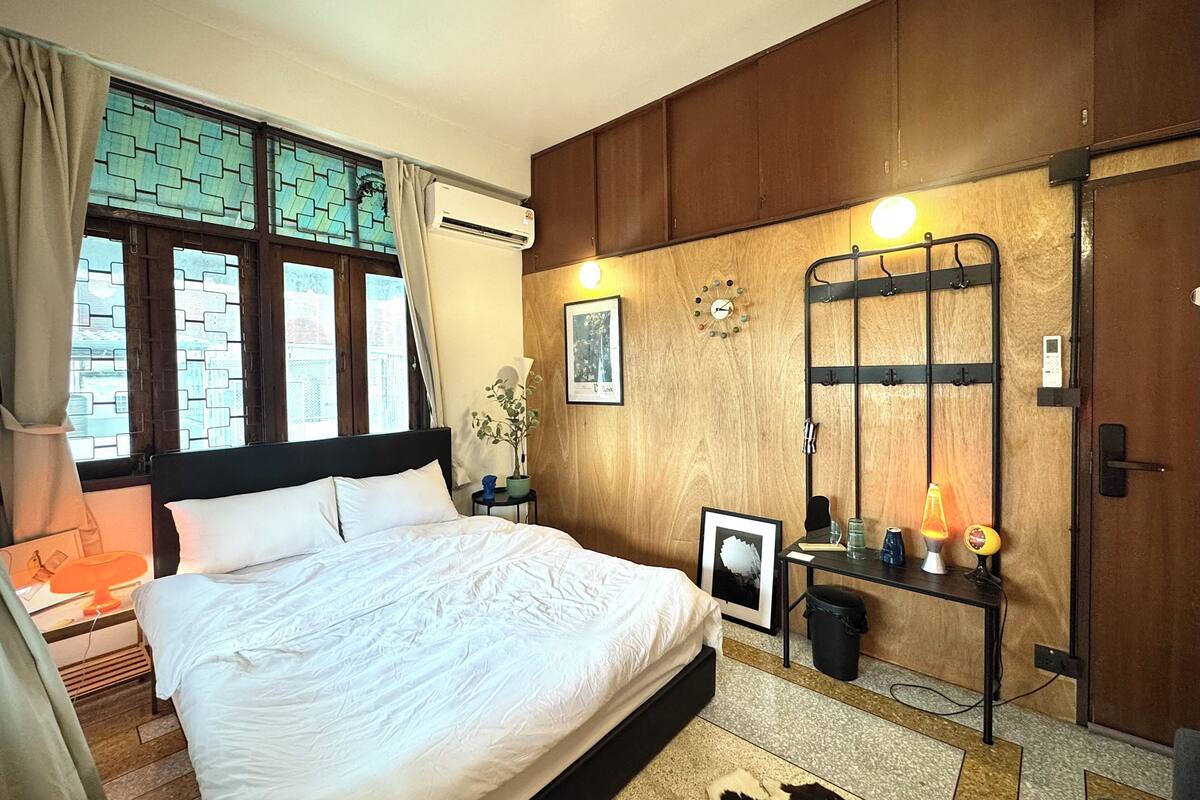 A bedroom with a bed, a nightstand, a potted plant, a wall clock, and a door.