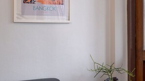 A framed cityscape poster of Bangkok on a wall, a grey sofa, and a small table with a plant.