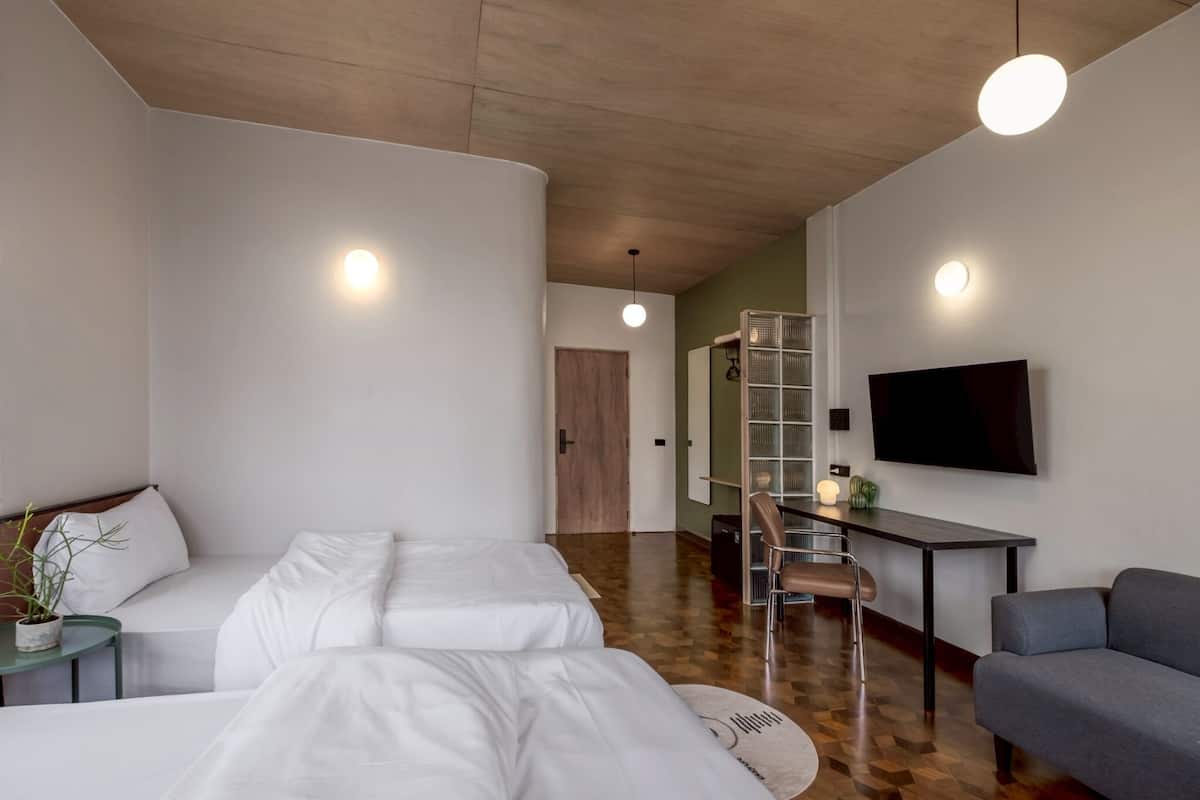 A modern hotel room with a large bed, a sofa, a desk, and a TV mounted on the wall.