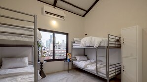 A dormitory room with bunk beds, a small table with a plant, and a window with a city view.