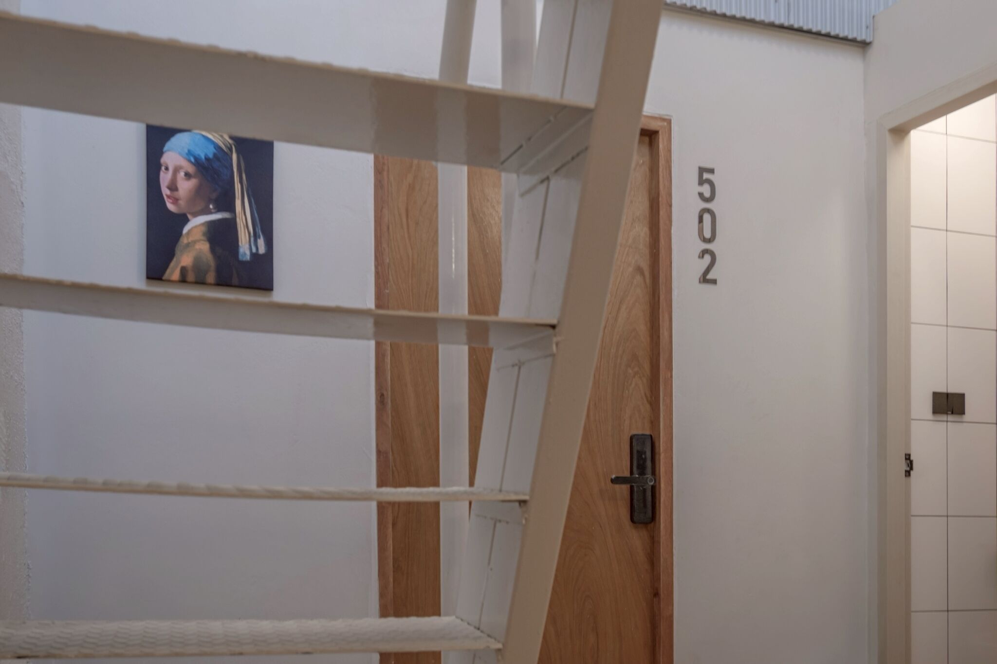 Una habitación con una puerta de madera marcada con el número 502, una pared blanca y un cuadro enmarcado sobre una repisa blanca.
