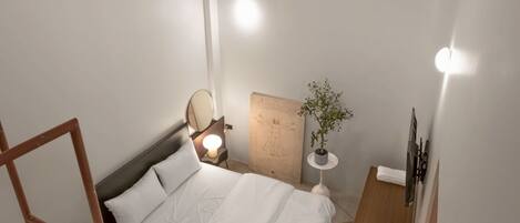 Et soveværelse med seng, sengebord, lampe og en lille potteplante.