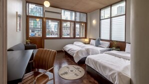 A hotel room with two beds, a desk, and a chair. There are large windows with a city view.