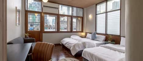 Habitación de hotel con dos camas, un escritorio y una silla. Amplias ventanas ofrecen vistas a la ciudad.