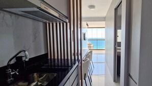 A modern kitchen with a black countertop, stainless steel sink, and a view of the balcony. - COBAR0129 - Edifício Barra Premium (Salvador)