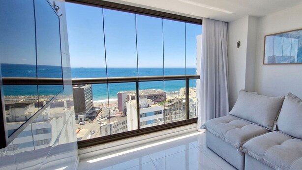 A modern living room with a large window offering a city view and a painting on the wall. - COBAR0129 - Edifício Barra Premium (Salvador)