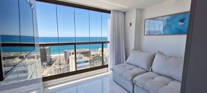 A modern living room with a large window offering a city view and a painting on the wall. - COBAR0129 - Edifício Barra Premium (Salvador)