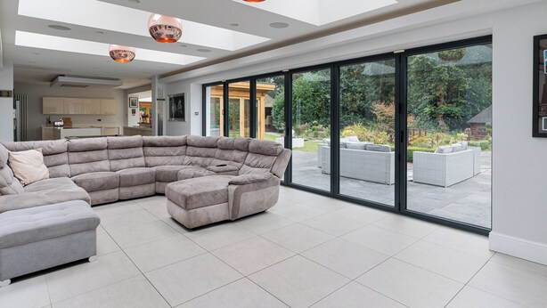 Amplia sala de estar con un sofá modular grande, un comedor y vistas al jardín a través de puertas correderas de vidrio.
