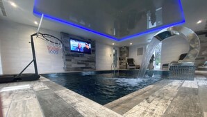 Una piscina interior con aro de baloncesto, una pantalla de televisión y una cascada.